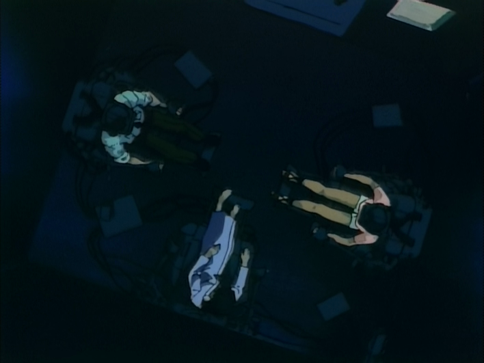 Anime screenshot, a top down perspective of three human actors attached to control devices.